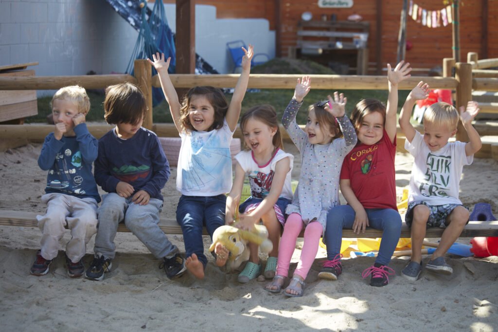 Seven happy preschool children sitting in a row in the playground